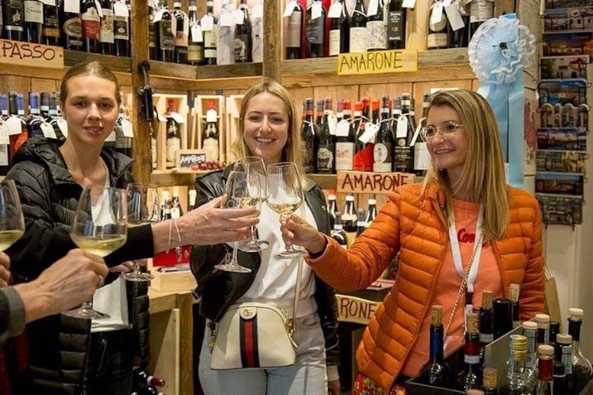 A group of people toasting with wine glasses in a store with shelves of wine bottles. 1