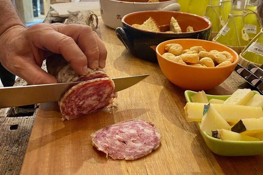 A person slicing salami on a wooden cutting board, surrounded by bowls of cheese and crackers. 2