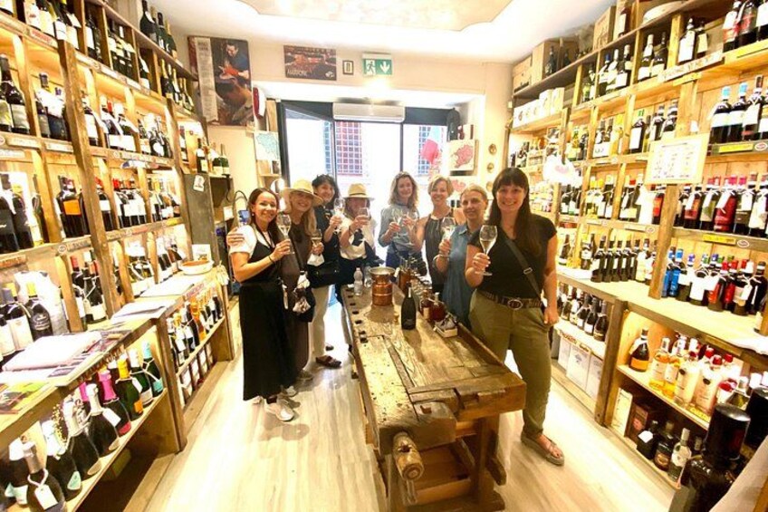 A wine shop with wooden shelves stocked with bottles, a central table, and a group of people. 5