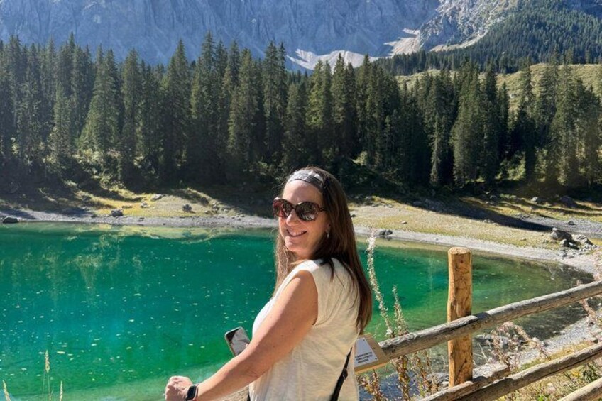 A person standing by a lake with a wooden railing, surrounded by a forest and mountains. 4