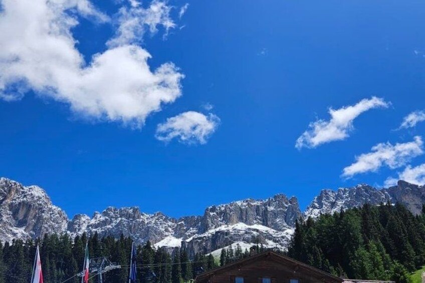 A mountain range with snow-capped peaks, a clear blue sky, and a forested area with a building in the foreground. 3
