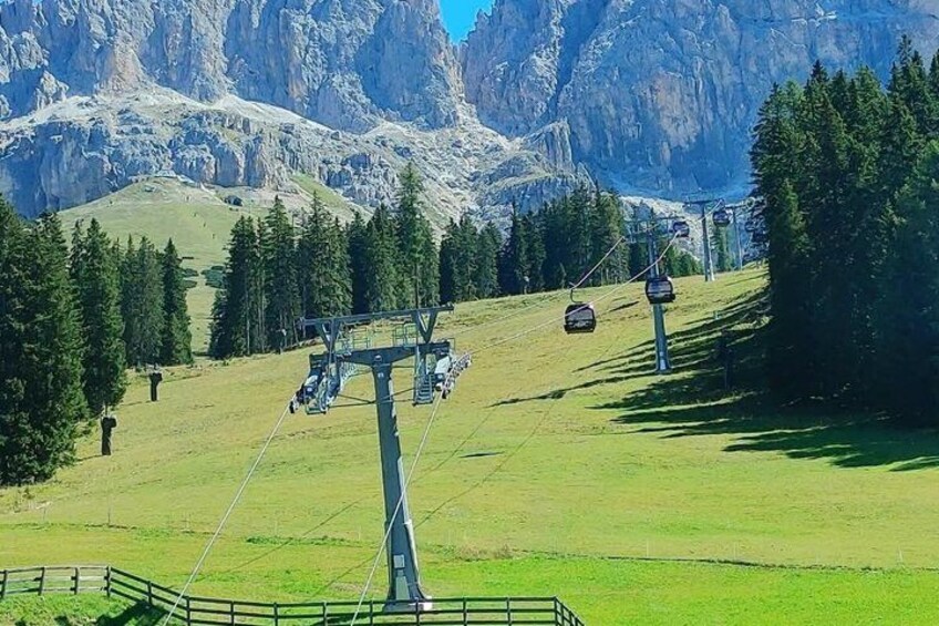 A ski lift with cables and chairs, a grassy slope, and a mountainous backdrop. 2