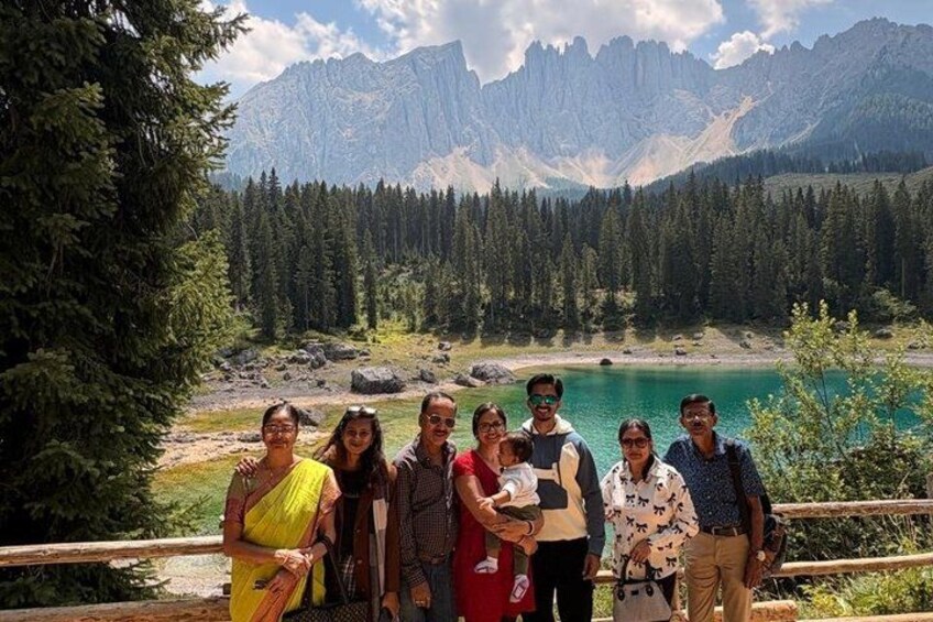 A group of people standing on a wooden platform with a mountainous landscape and a lake in the background. 1