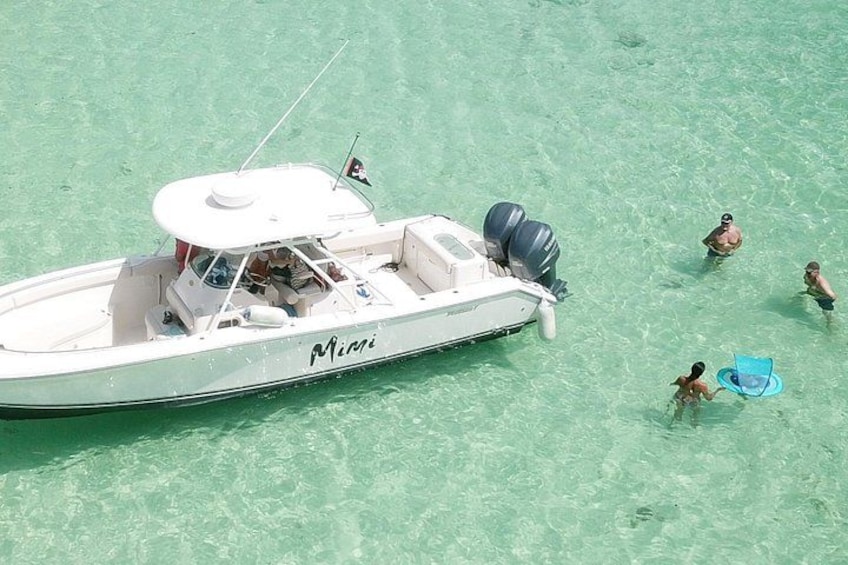 Un bote blanco llamado 'Mimi' en aguas turquesa cristalinas, con gente nadando y un niño con un flotador azul. 2