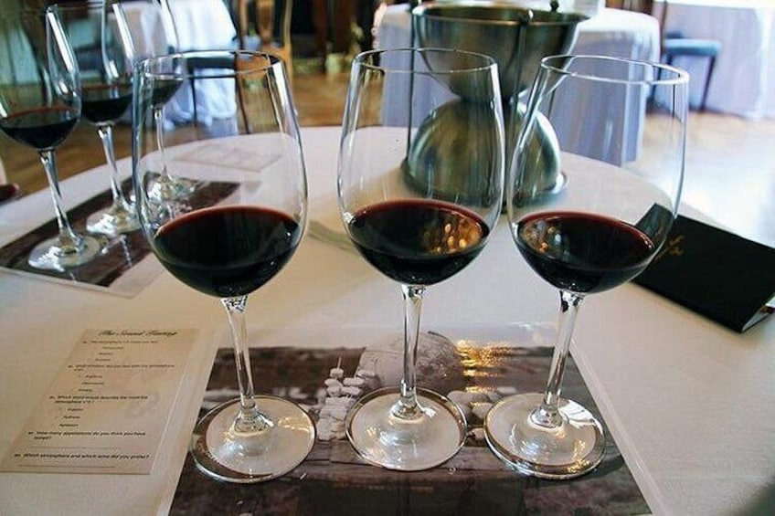 Trois verres à vin remplis de vin rouge sont posés sur une table, à côté d’un menu. 1