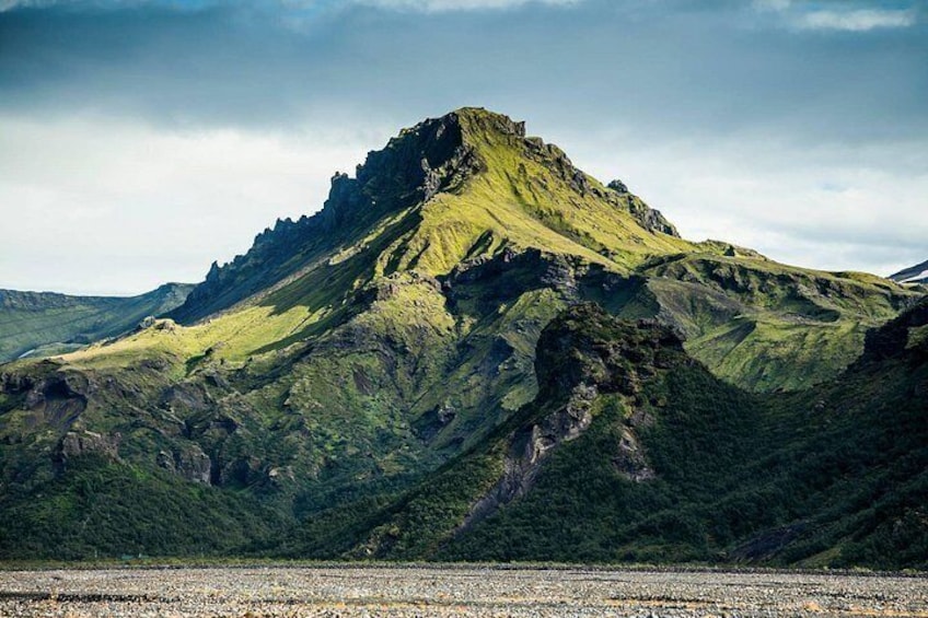 Una montaña con un pico destacado, rodeada de colinas verdes y un primer plano con grava. 1