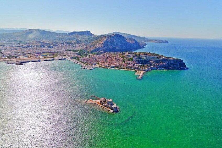 Vista aérea de una ciudad costera con una isla destacada, aguas azules cristalinas y un helicóptero aterrizando en un muelle. 4