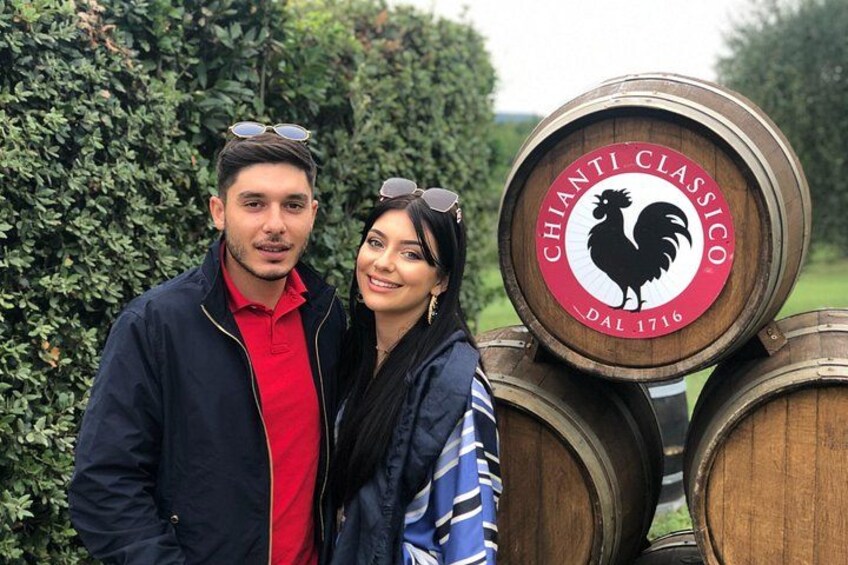 Dos personas de pie frente a barriles de madera con un logo de gallo y el texto 'CHIANTI CLASSICO dal 1716'. 1