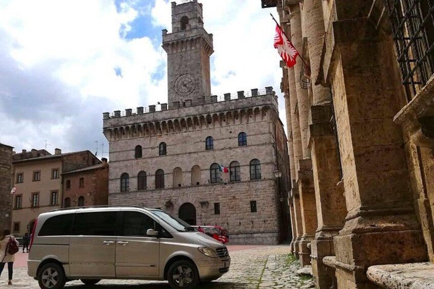 A beige minivan parked in front of a historic building with a clock tower. 2