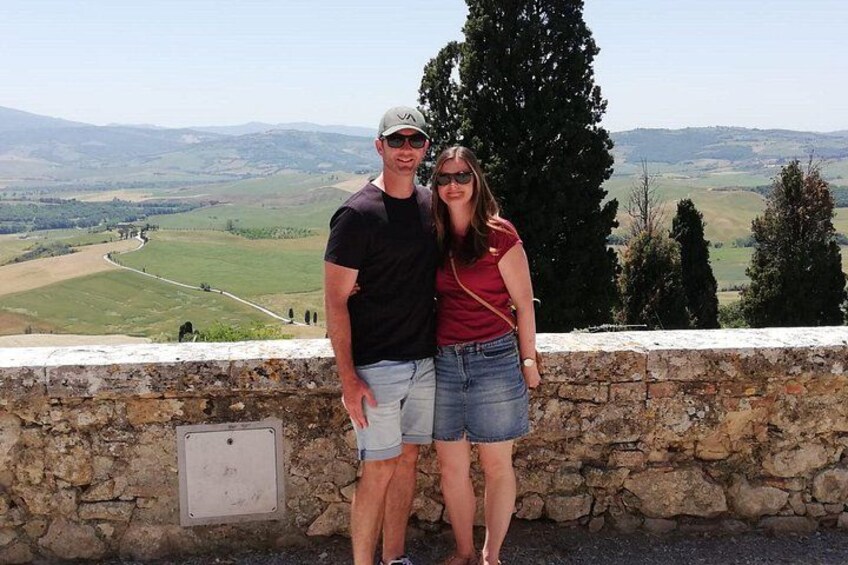 A couple standing on a stone wall overlooking a valley with rolling hills and a winding road. 5