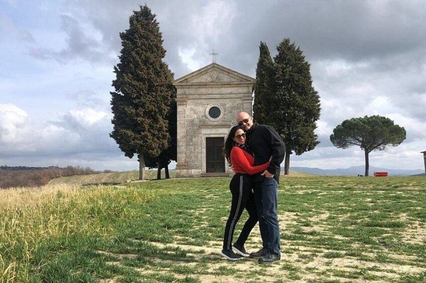 Una pareja abrazándose frente a un edificio histórico con dos árboles altos y un cielo despejado. 4