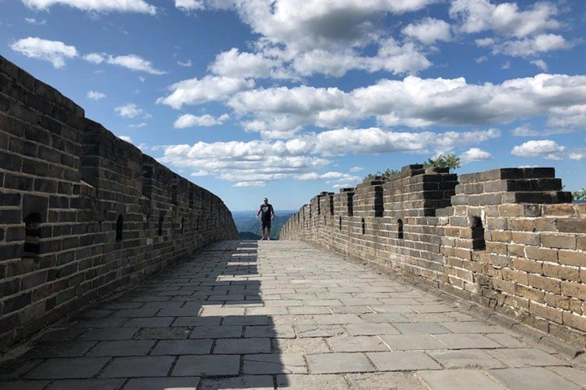 A long, straight pathway flanked by high stone walls, leading towards a distant horizon under a partly cloudy sky. 3