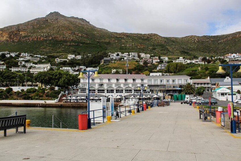 A coastal pier with a white building, a mountain, and houses in the background. 2