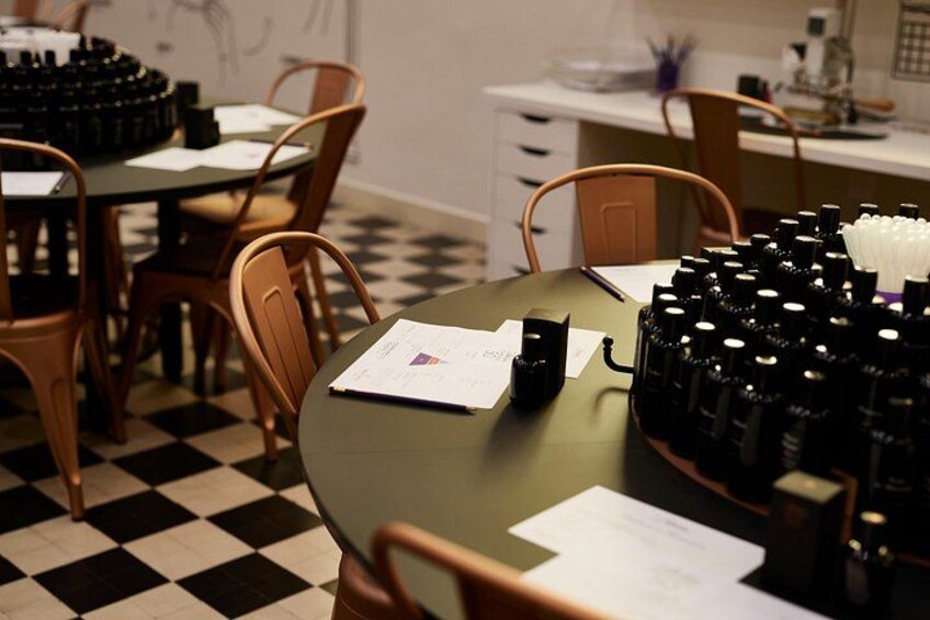 Une pièce avec un sol à carreaux, une table recouverte de papiers et un appareil noir, ainsi que des chaises disposées autour de la table. 2