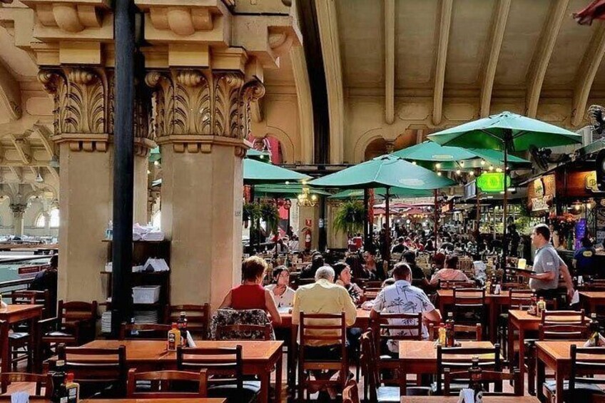 An indoor dining area with wooden tables and chairs, green umbrellas, and columns. 3