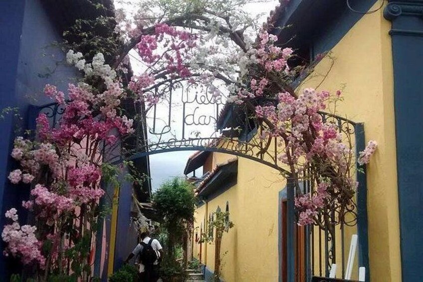 Ein schmaler Gang mit rosa und weißen Blüten, einem Metallgitter und einem gelben Gebäude. 2