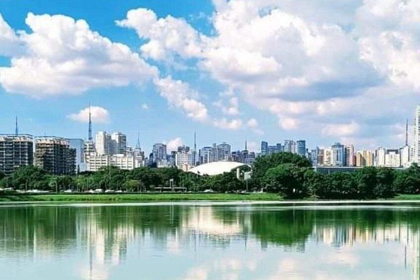 A city skyline with a large stadium, a body of water reflecting the buildings, and a clear sky. 4