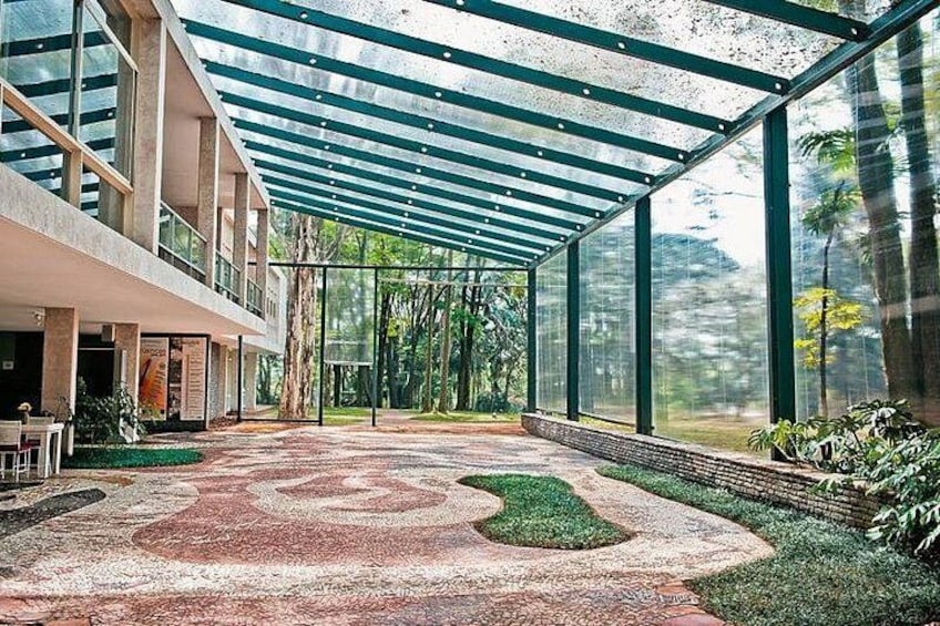 Un espace extérieur abrité, doté d’un chemin pavé à motifs, de murs en verre et de verdure. 3