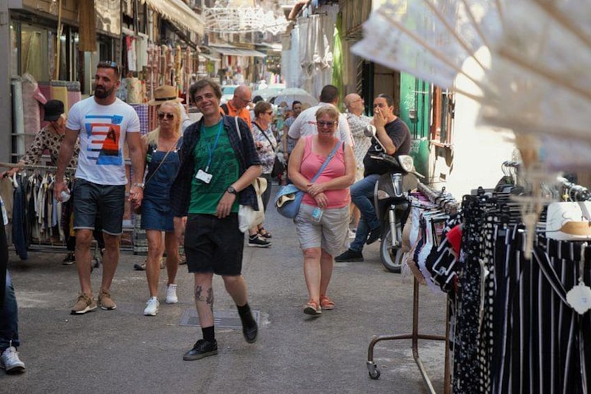 Ein belebter Markt mit vielen Menschen, die flanieren, und Händlern, die Kleidung anbieten. 3