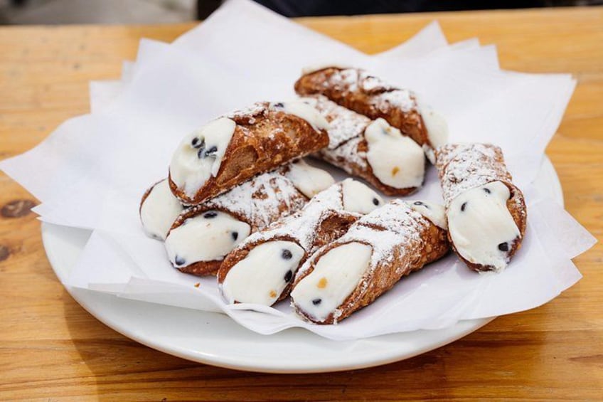 Ein Teller mit Cannoli, gefüllt mit weißer Creme und Schokoladenstückchen, bestäubt mit Puderzucker. 2
