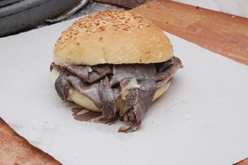 A sandwich with a sesame seed bun, meat filling, and a white sauce. 2
