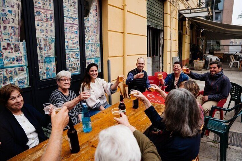 A group of people sitting around a wooden table outdoors, toasting with drinks. 3