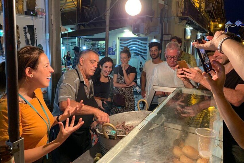 Un groupe de personnes se trouve devant un étal de nourriture, avec un présentoir et un comptoir. 1