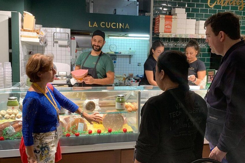A food counter with a display case, a person wearing a black shirt with text, and another person in a blue top. 2