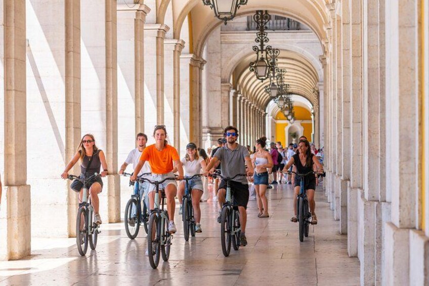 A group of people riding bicycles on a wide, covered walkway with arches and columns. 4