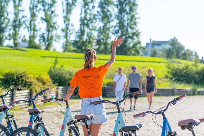 A person in an orange shirt with a cycling website on the back, standing in front of bicycles. 3