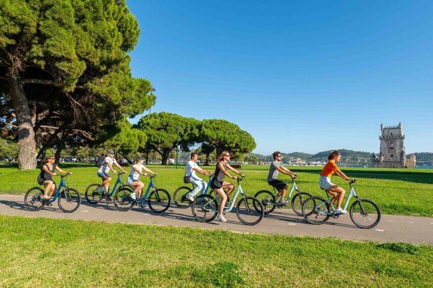 A group of people riding bicycles on a path in a park with trees and a distant castle. 5