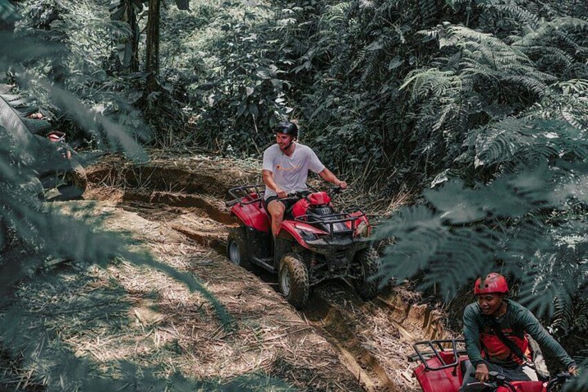 A person riding a red ATV in a forested area with dense foliage. 4