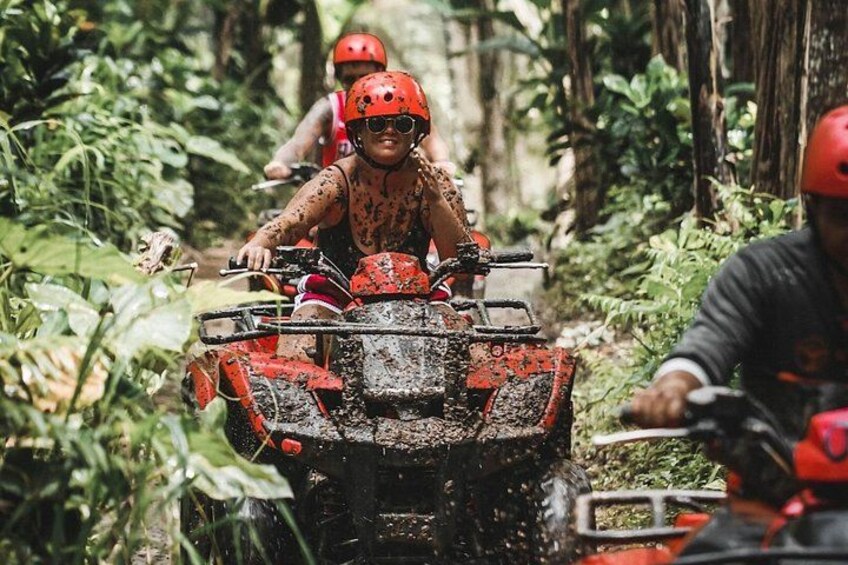 Two people riding a red ATV through a forested area. 2