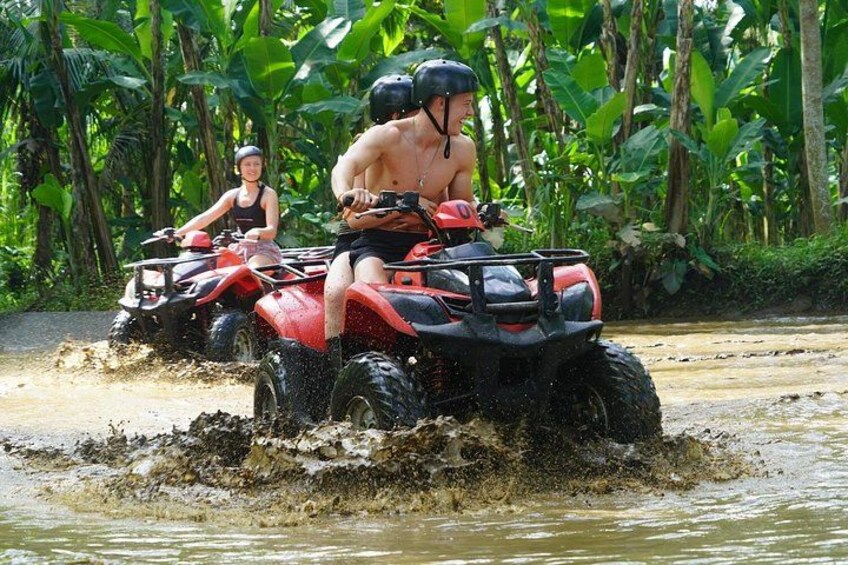 Twee personen op rode terreinvoertuigen (ATV's) rijden door een modderige waterovergang. 5