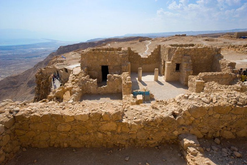 Des ruines antiques aux murs et aux colonnes de pierre, se dressant au milieu d’un vaste paysage désertique, avec des montagnes lointaines à l’horizon. 4