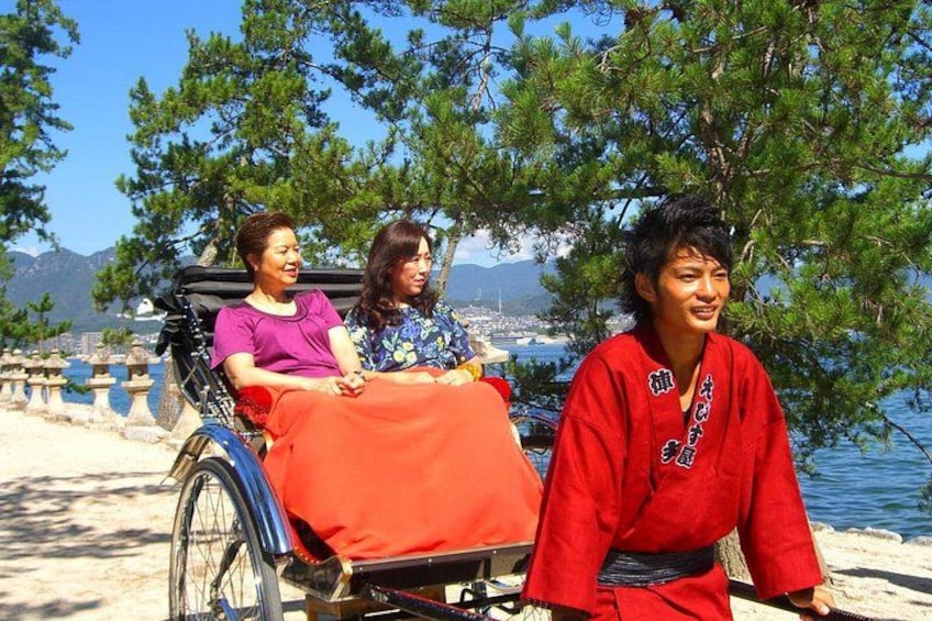 A person in a red traditional outfit sitting on a wheelchair by a lakeside with trees and mountains in the background. 2