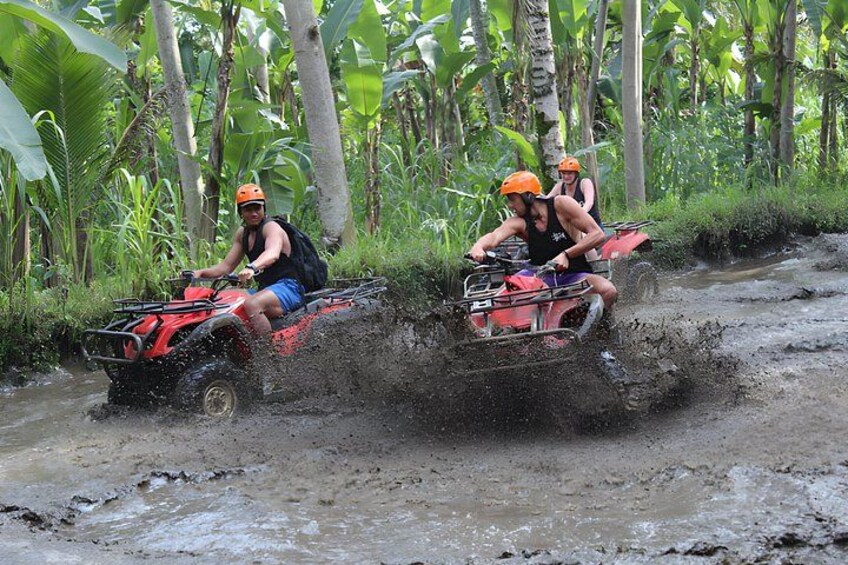 Two people on a red ATV navigating through a muddy path in a tropical forest. 3