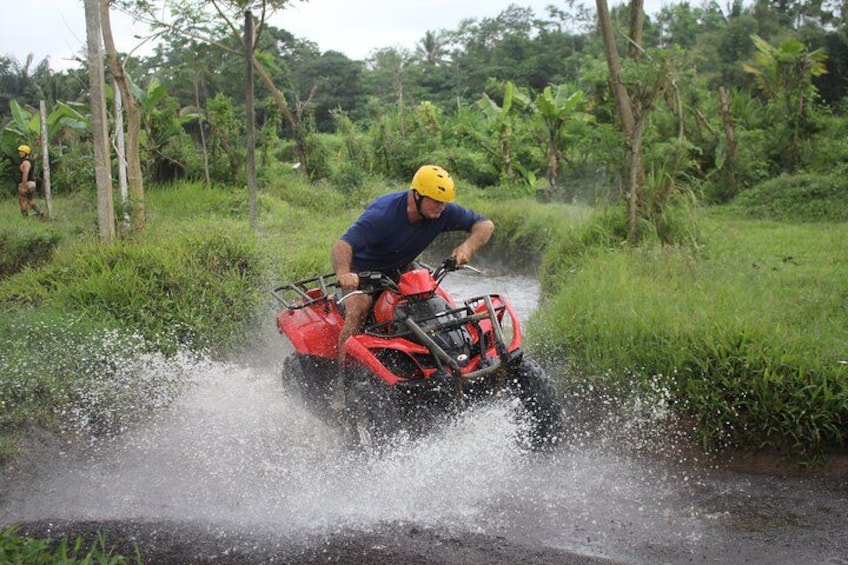 A person riding a red ATV through a water channel, splashing water. 3