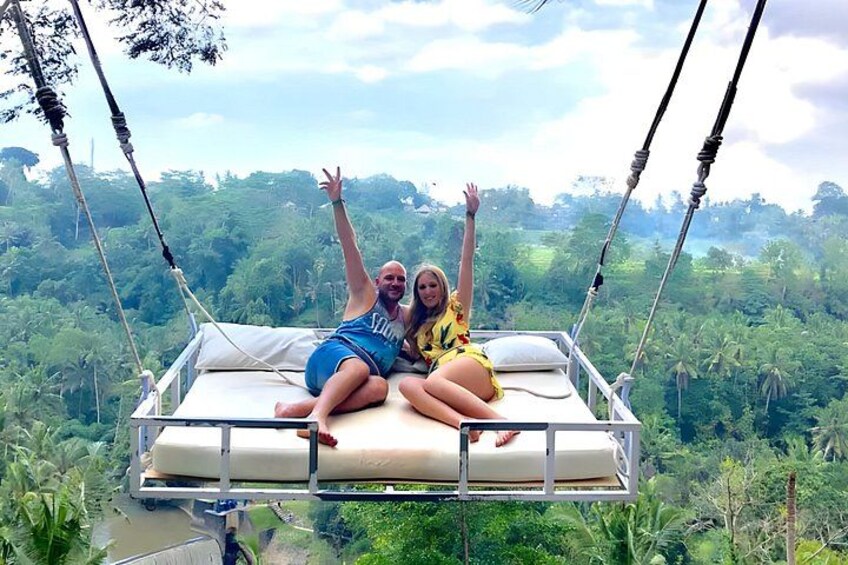 Two people on a suspended bed with a jungle landscape in the background. 3