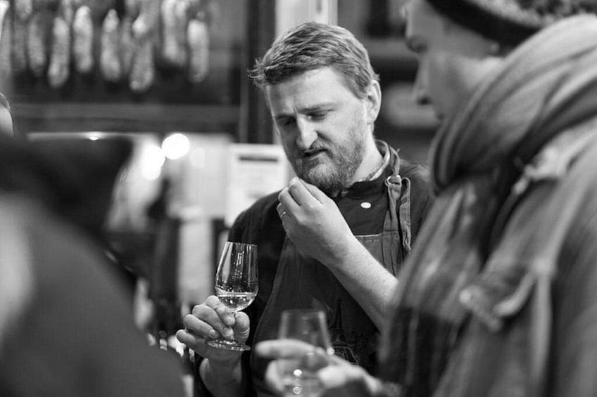 A person holding a wine glass, another person with a blurred face, and a bar setting with bottles in the background. 2