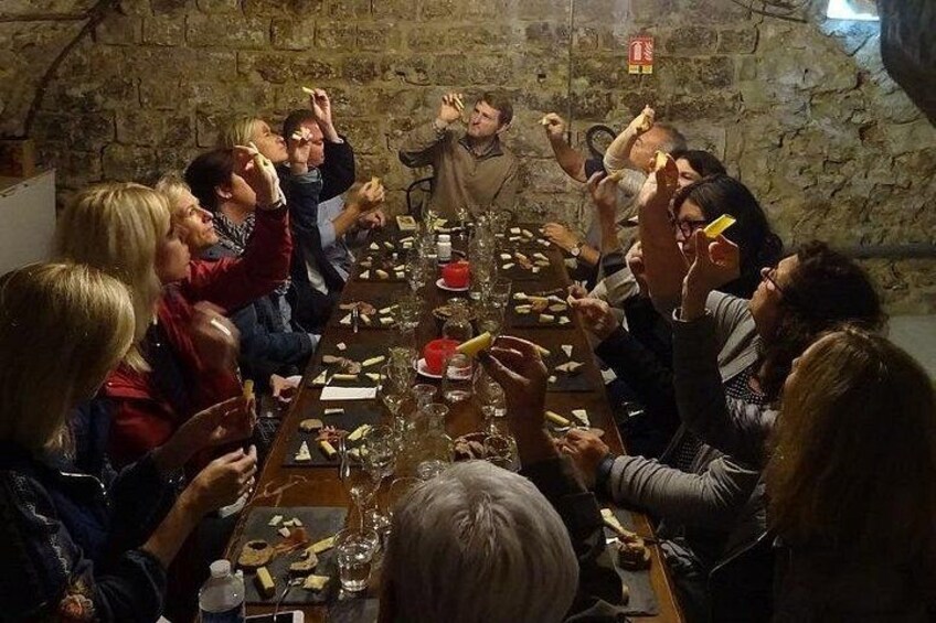 Un gruppo di persone attorno a un lungo tavolo in una stanza con pareti in pietra, brindano con bicchieri e cibo. 2