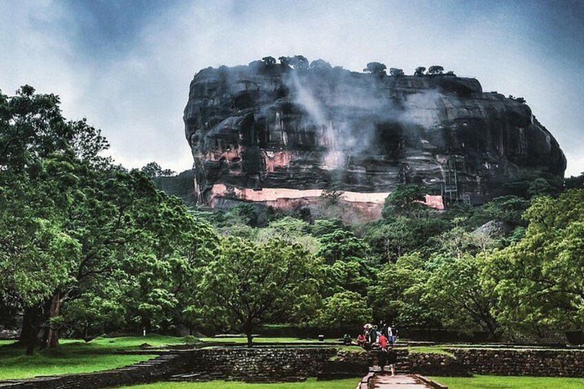 A large rock formation with trees in the foreground and a cloudy sky. 2