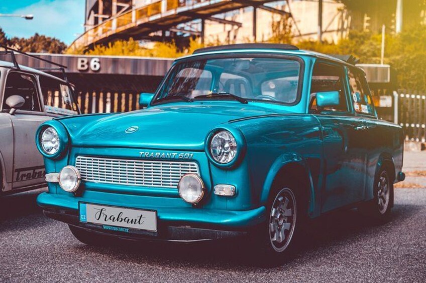 En turkis Trabant 601 bil parkeret på en gade med en bro og træer i baggrunden. 1