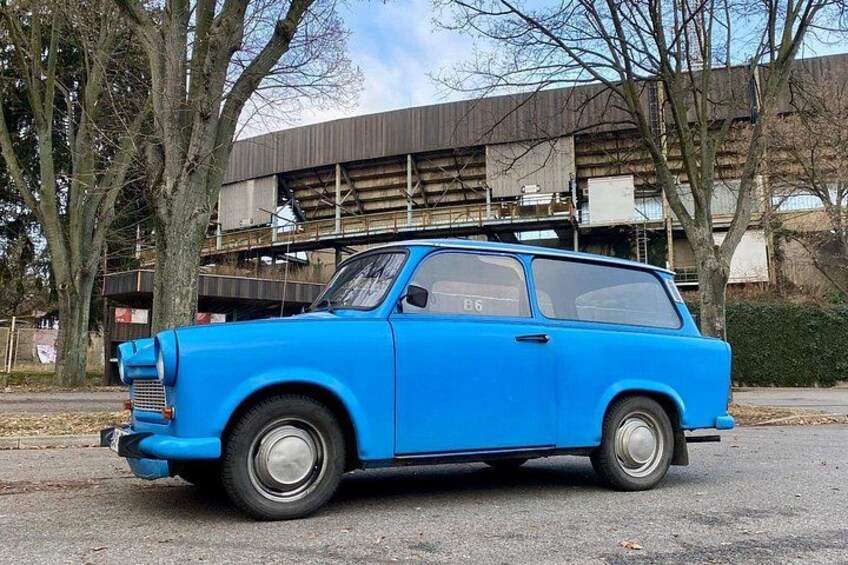 En blå, klassisk bil parkeret på en gade med træer og en bygning i baggrunden. 4