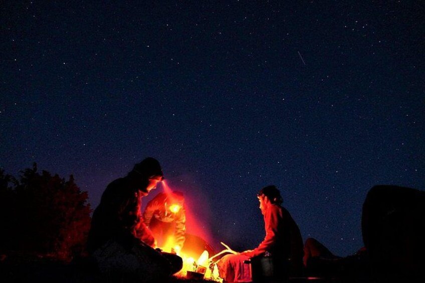 Two people sitting by a campfire under a starry night sky. 3