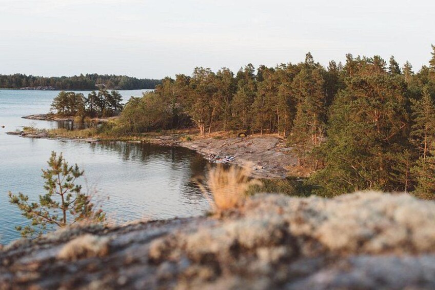 A forested shoreline with a calm lake, rocky terrain, and a distant tree line. 2