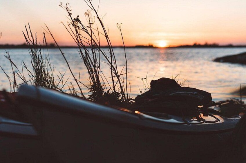 A sunset over water with grass and a backpack. 4
