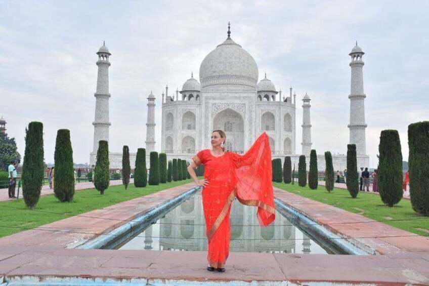 A person in a red dress standing in front of the Taj Mahal with its reflection in the water. 5