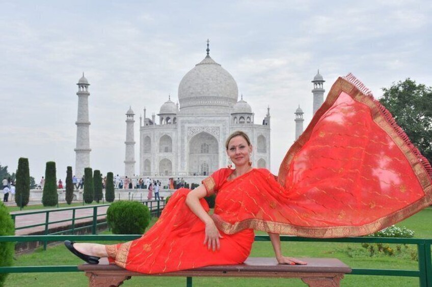A person in a red dress sitting on a bench with the Taj Mahal in the background. 4