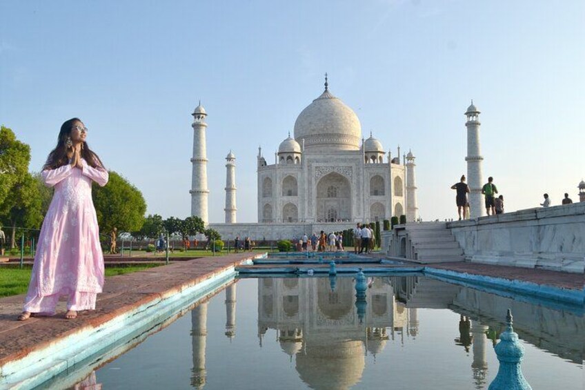 The Taj Mahal with a person in a pink dress in the foreground and a reflection in the water. 4